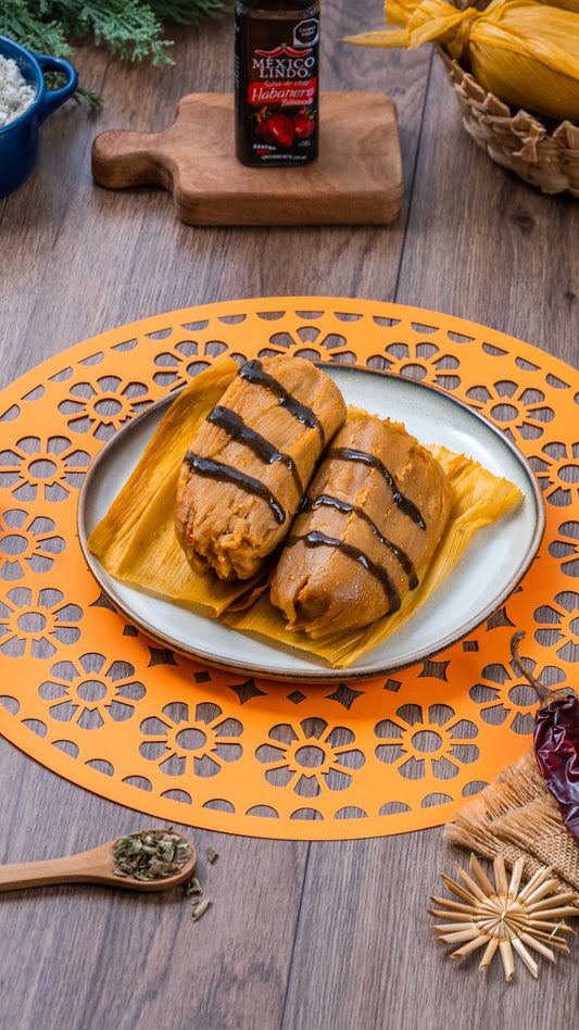 Tamales de puerco bañado en Salsa México Lindo Habanero Tatemado® sobre un plato decorado en una mesa