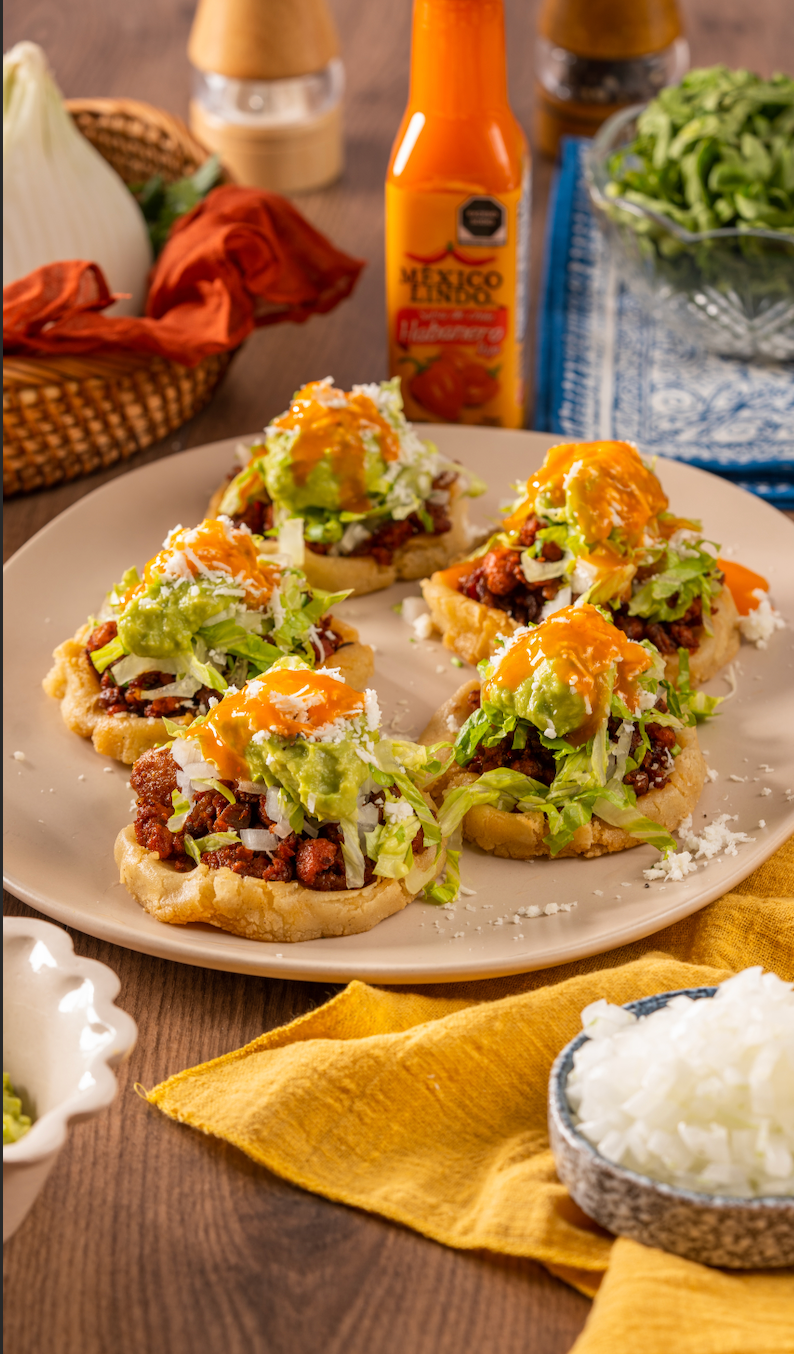 Sopes de chicharrón con chorizo, frijoles refritos, coronados con cebollita blanca, lechuga, cilantro y queso cotija bañados en Salsa México Lindo Habanero Rojo®️